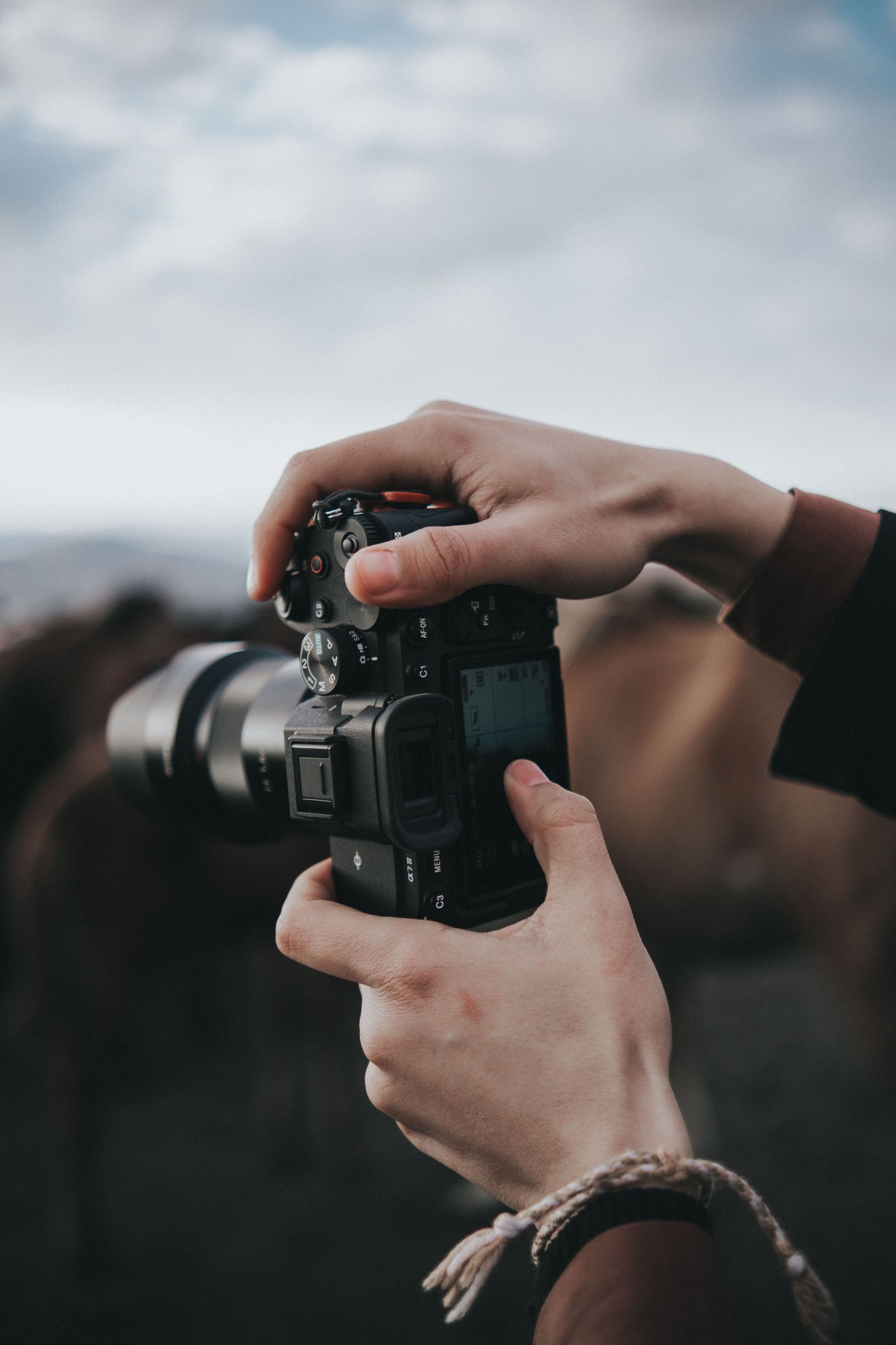 Hands gripping a camera, capturing the moment outdoors with a blurred background.